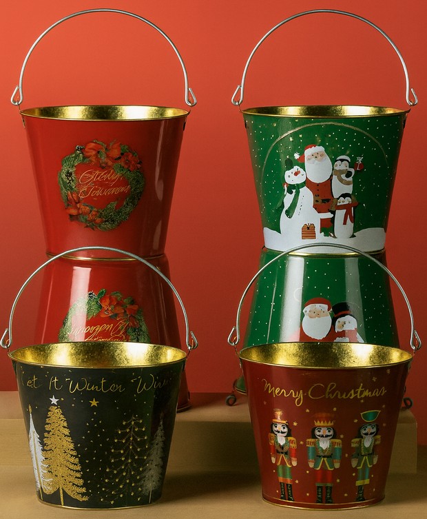 Four Christmas-themed metal buckets with festive designs on a wooden surface against an orange wall.