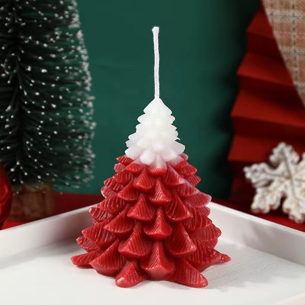 Red and white Christmas tree-shaped candle on a white surface with a green and red background.