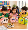 Three children sitting at a table in a classroom, eating from colorful cartoon lunch boxes and drinking from matching water bottles. The products shown include a pink owl lunch box with a pink bottle, a green monster lunch box with a blue bottle, and a white cat lunch box with a pink bottle.